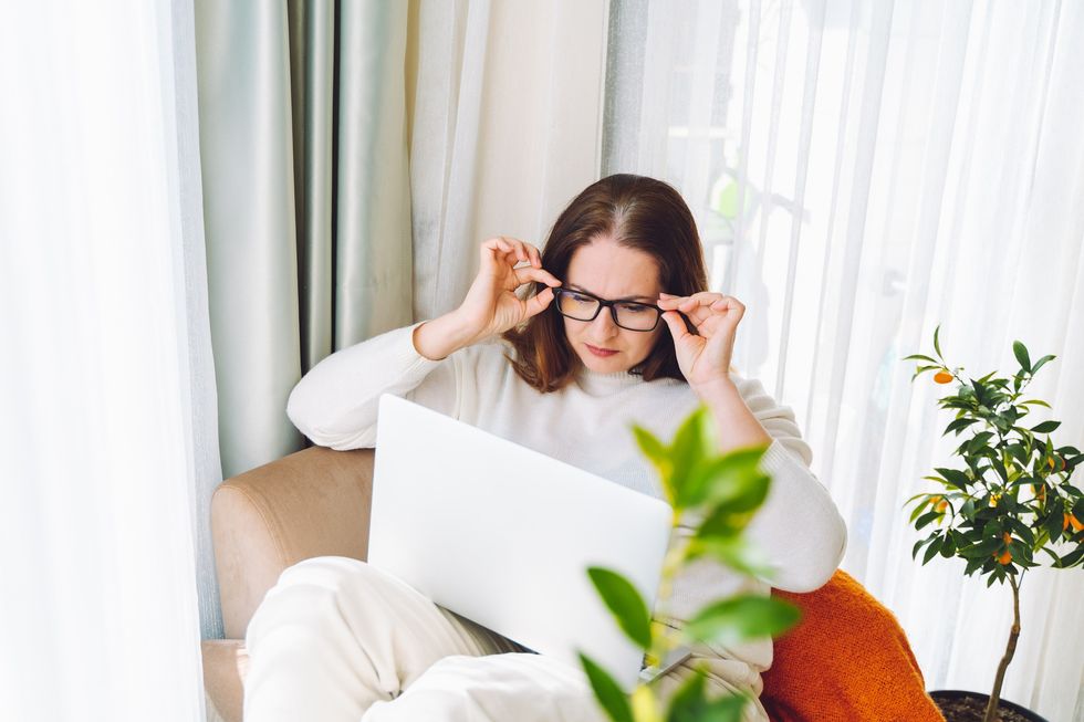 Woman wearing glasses, squinting to read something on laptop