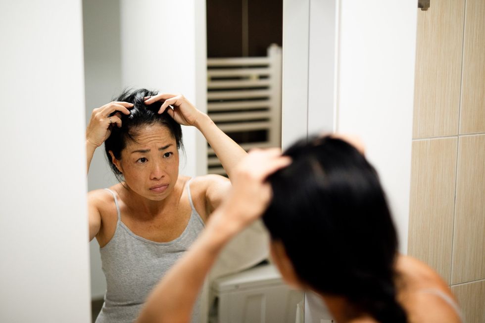 Woman with black hair, checking for hair loss in bathroom mirror