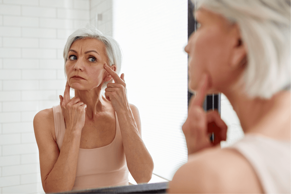 Woman with grey hair looking at her skin in the mirror
