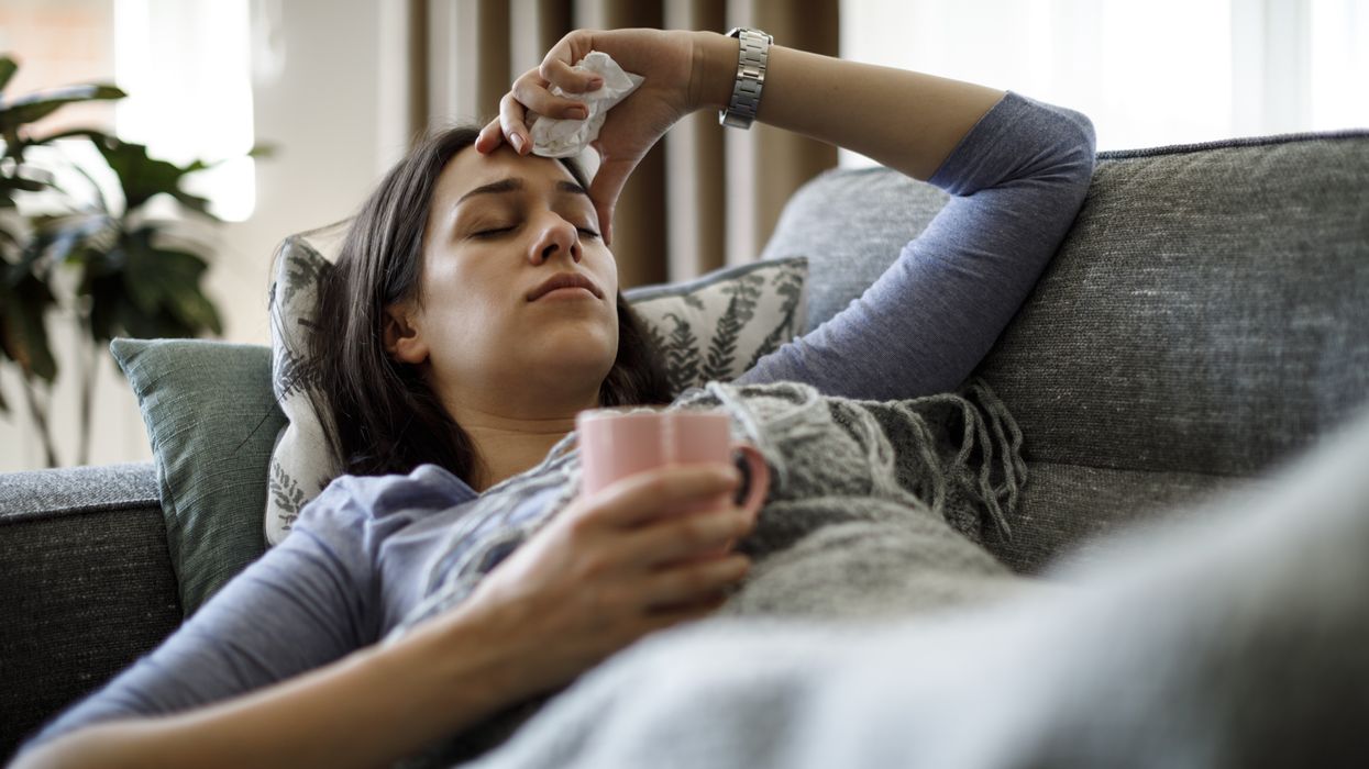 Woman with the flu holding her head and wrapped in a blanket on the sofa