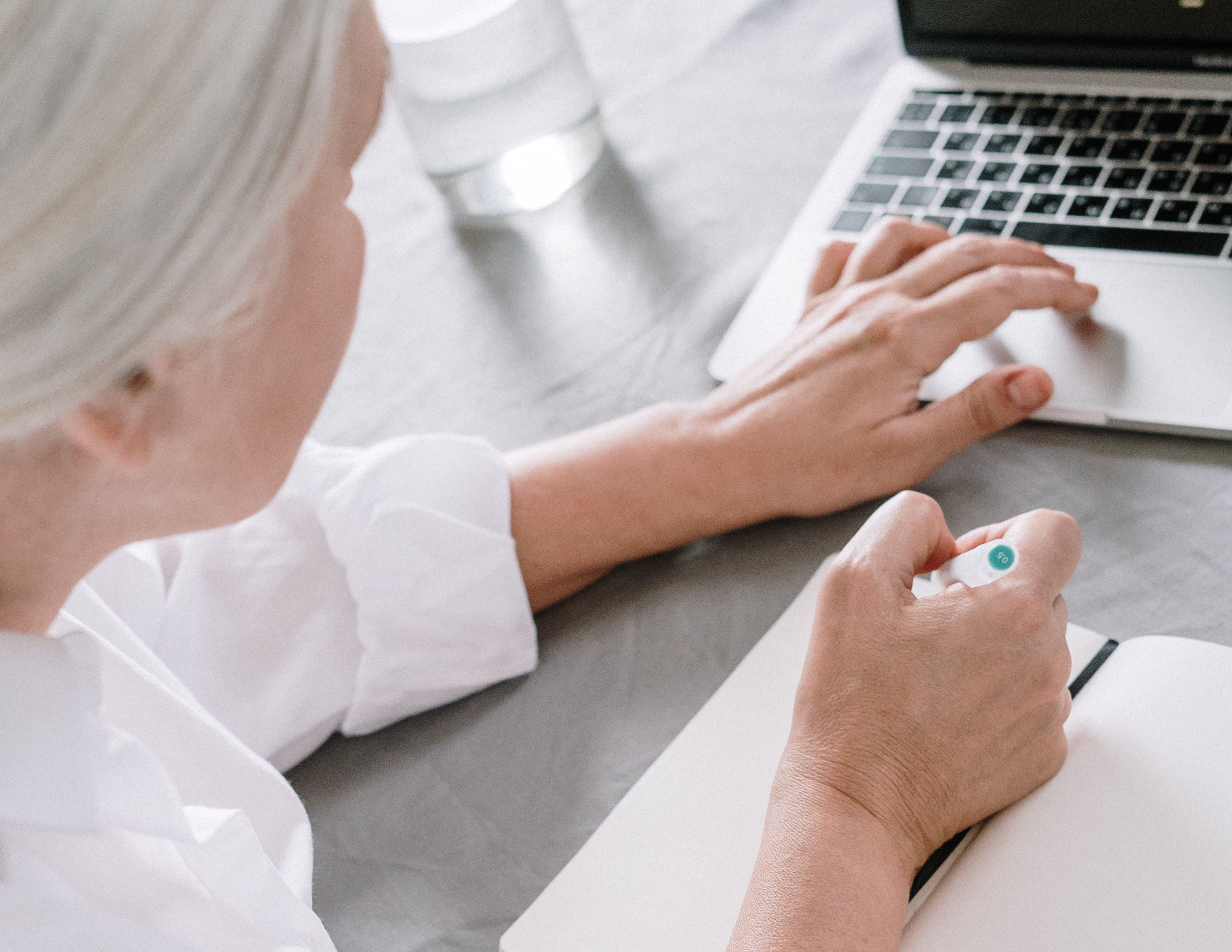 Woman writing on a notepad while her hand is on a laptop
