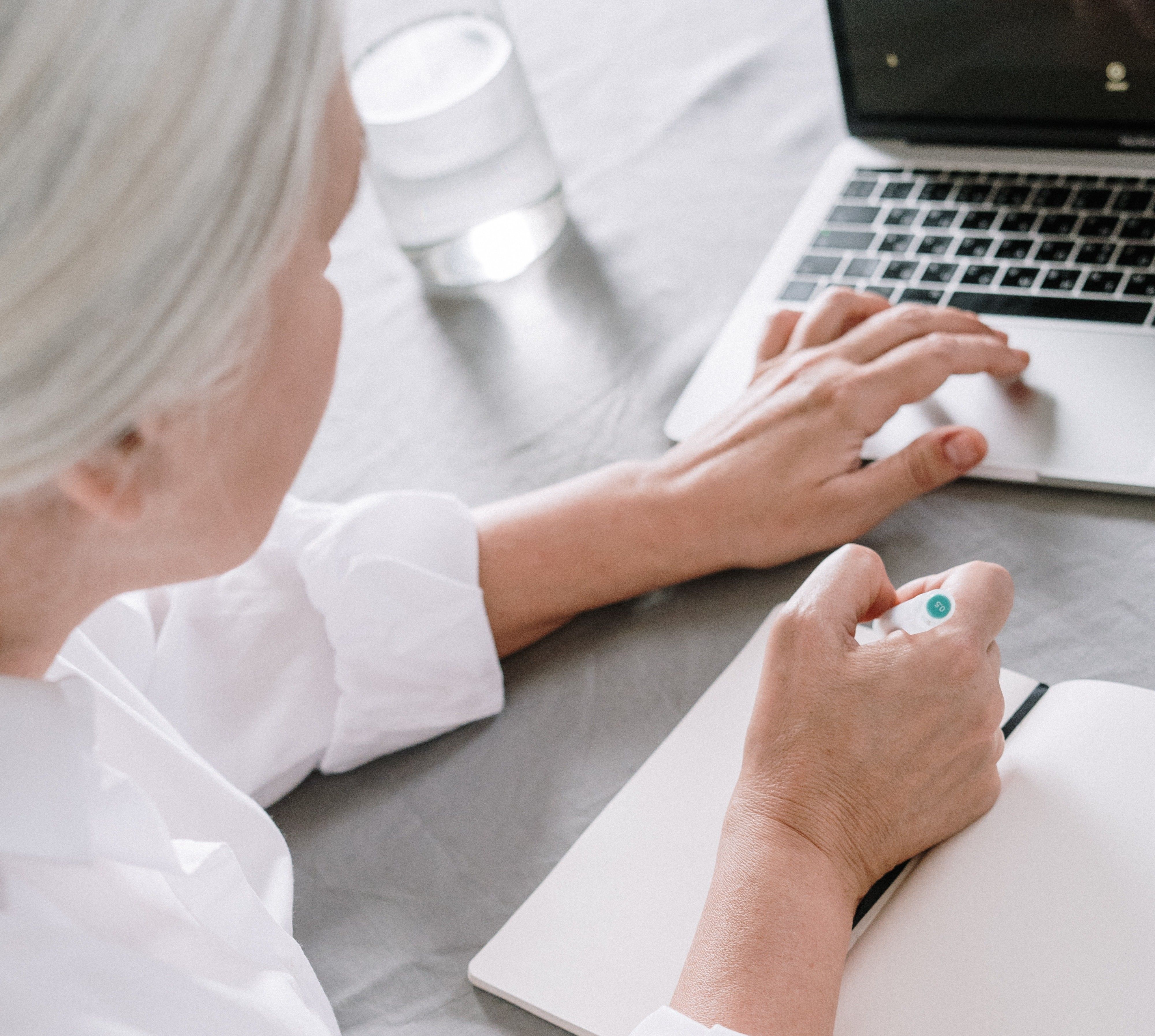 Woman writing on a notepad while her hand is on a laptop