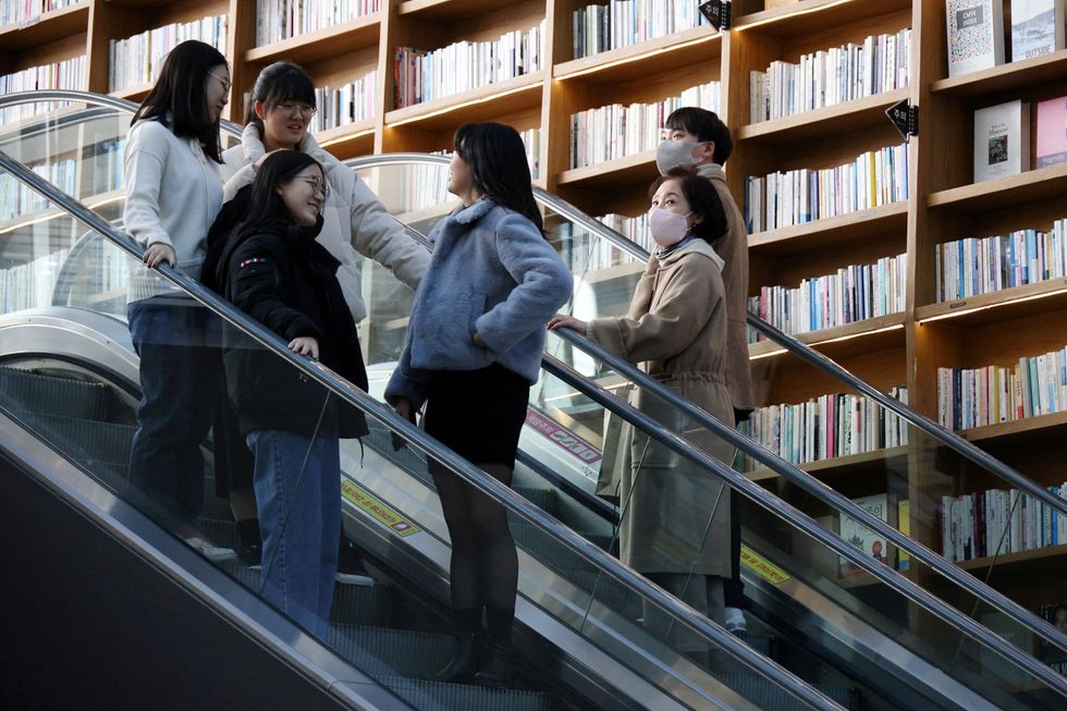 Women ride on an escalator past a couple wearing masks to avoid contracting the coronavirus disease (COVID-19) at a shopping mall in Seoul, South Korea, January 30, 2023. REUTERS/Kim Hong-Ji