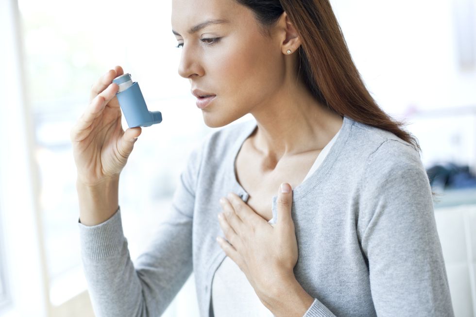 Young woman using an inhaler and touching her chest